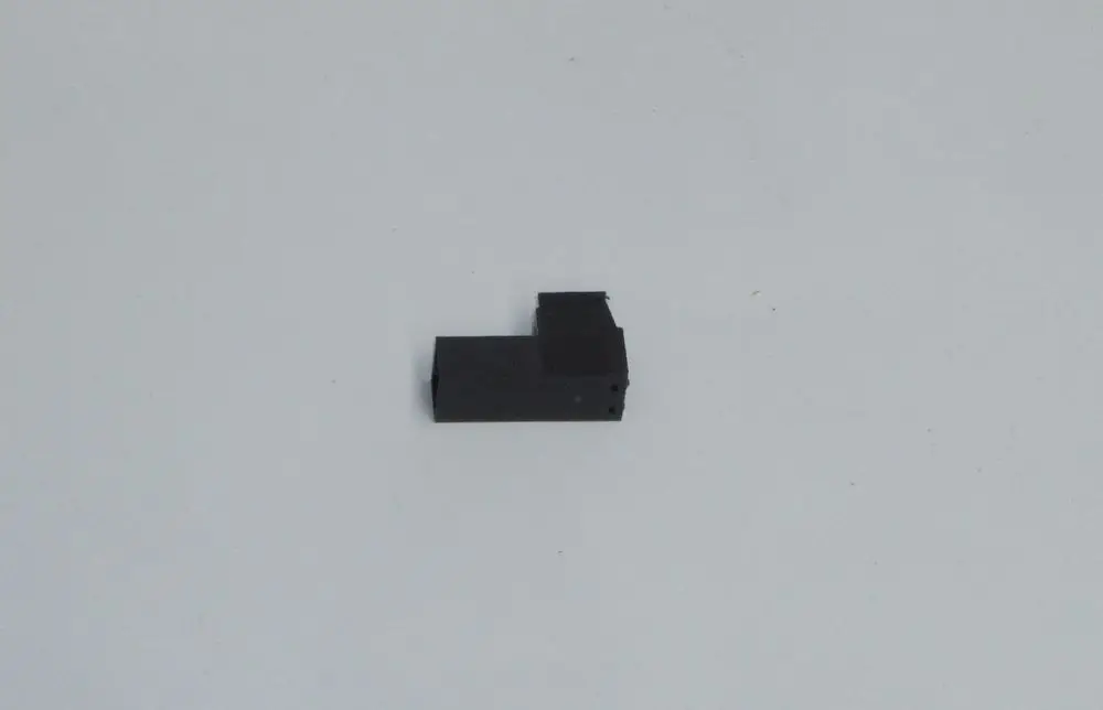 Schwarzer Stecker mit einer L-förmigen Struktur, liegend auf einem hellen Untergrund. Das Produkt gehört zur Marke Daikin.